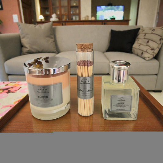 Cakaza Amber candle, reed diffuser, and branded matches arranged on a wooden tray in a cozy living room
